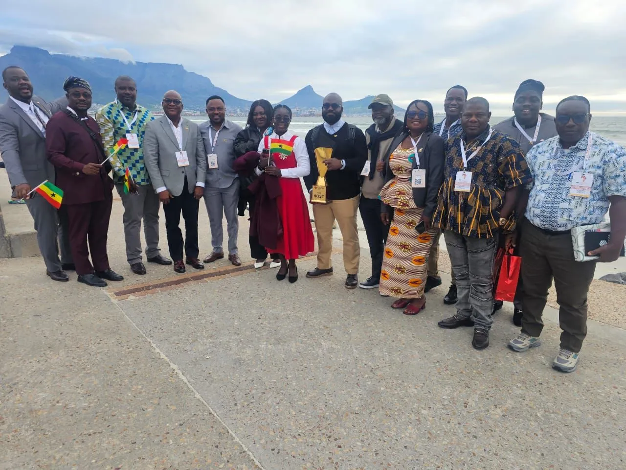 La délégation ghanéenne à l'édition du Cap de la SASCON, réunie sur le front de mer devant la montagne de la Table, tenant le trophée d'hôte et de petits drapeaux du Ghana.